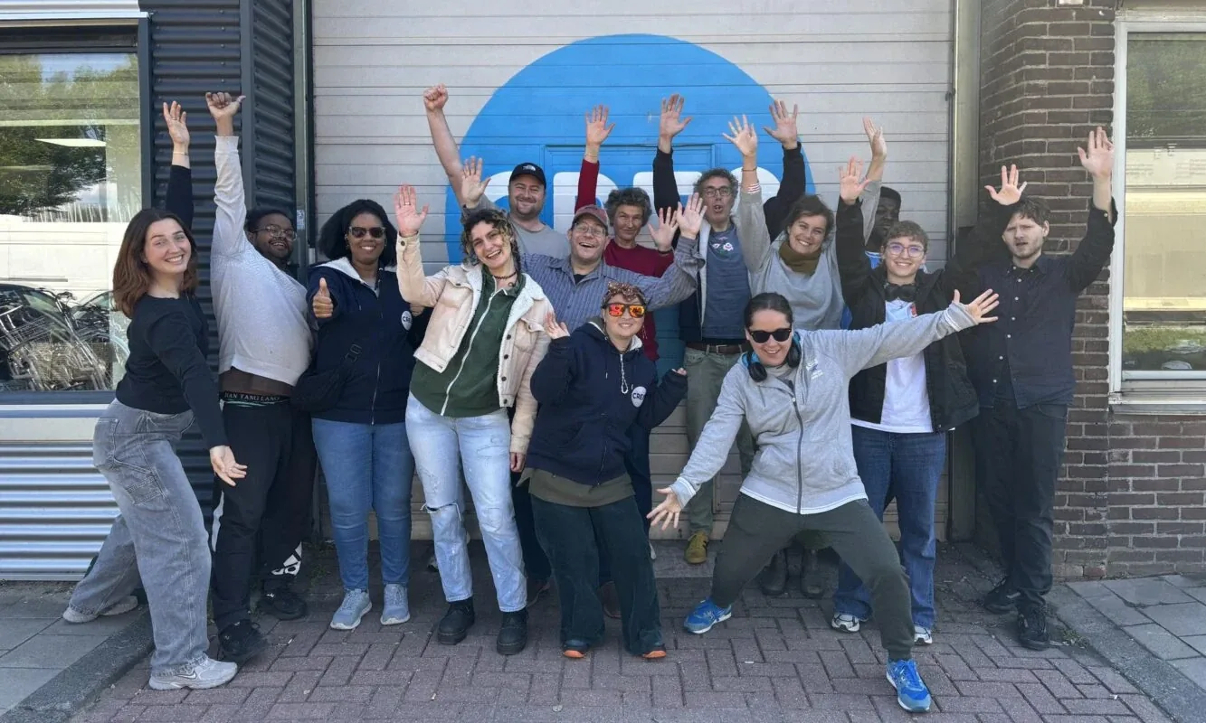 Medewerkers van CRE8, een sociale werkplaats in Amsterdam, zwaaien met opgestoken handen in de camera